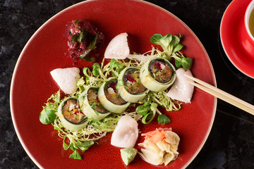 Sushi roll with salmon, avocado, tuna fish, sesame and cream cheese served on red plate with fresh lettuce on black marble background