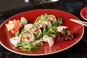 Sushi roll with salmon, avocado, tuna fish, sesame and cream cheese served on red plate with fresh lettuce on black marble background