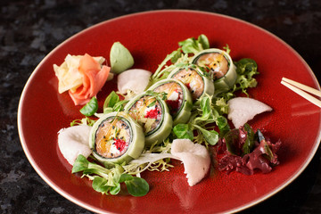 Sushi roll with salmon, avocado, tuna fish, sesame and cream cheese served on red plate with fresh lettuce on black marble background