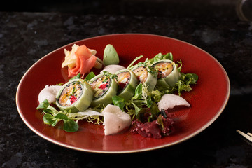 Sushi roll with salmon, avocado, tuna fish, sesame and cream cheese served on red plate with fresh lettuce on black marble background