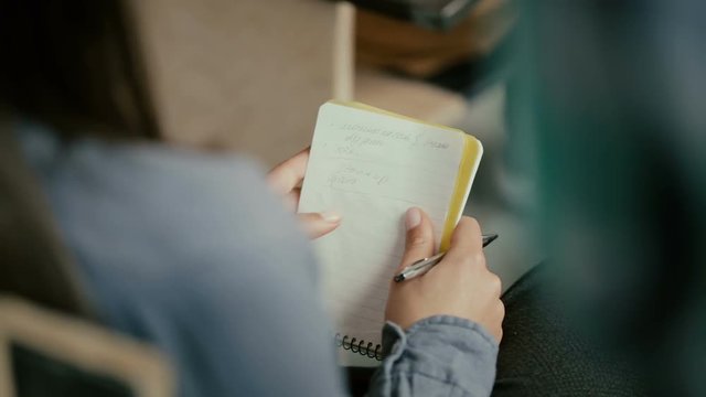Close-up view of female hands. Woman sitting on a chair and writing in notebook. Student talking with people at lecture.