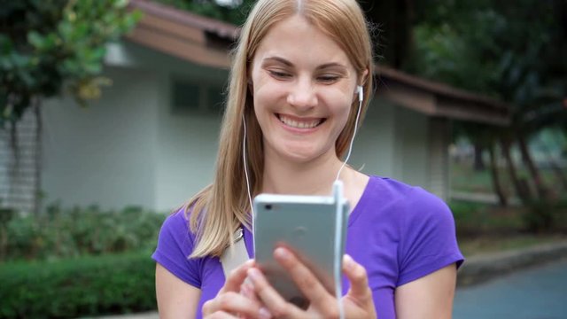 Beautiful girl walking in a park, smiling and talking with friends on her smart phone by skype