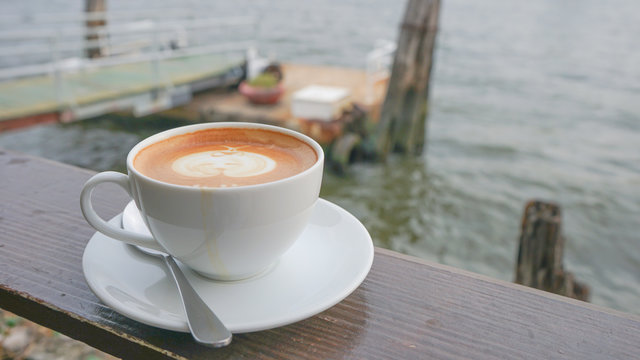coffee cup shisu dog latte art on wooden table in coffee shop or restaurant by pier river / coffee cup blur background
