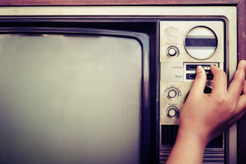 Woman hand fine tuning vintage television with control button. Retro image processed.