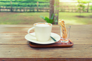Coffee cup and pastry on wooden table with nature background.