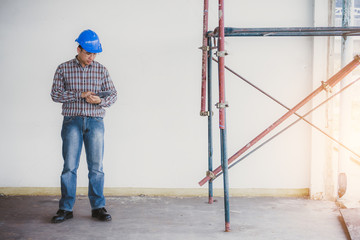 Portrait of confident foreman standing and holding tablet with safety helmet and scaffolding on old buildings in his job site.