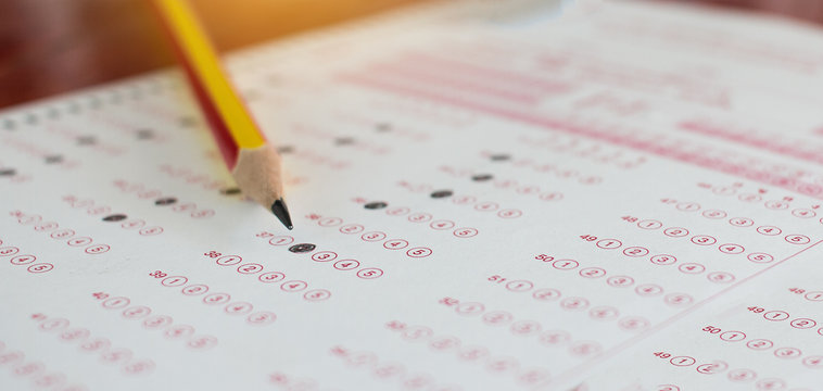 Standardized test exams form with answers bubbled in and color pencil resting on the paper test, education concept