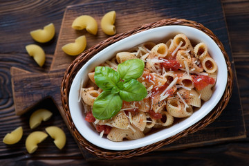 Above view of boiled pasta shells with tomato sauce and cheese on a rustic wooden background, studio shot