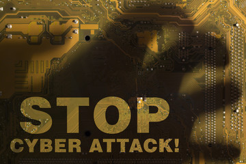 The inscription "Stop cyber attack" through the shadow of the hand on the yellow motherboard.