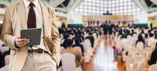 businessman using the tablet, blurred of conference hall or seminar room with attendee background. business or education concept.