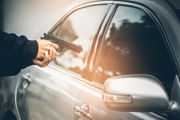 A robber dressed in black pointing a gun at a driver in a car. Car thief concept.