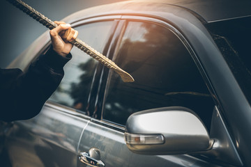 A robber dressed in black holding crowbar at a driver in a car. Car thief concept.