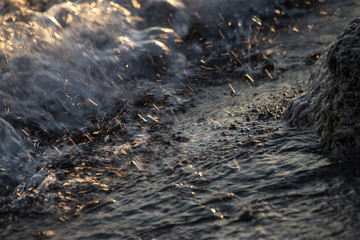 A close shutter of water splashing on the rocks, with details of bubbles and sparkles reflecting light at sunset