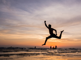 Fototapeta na wymiar silhouette happiness man jump during sunset or sunrise while on holiday at the beach.