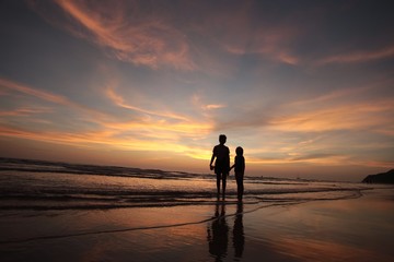 Fototapeta na wymiar silhouette of mother and child walking on the tropical beach sunset background