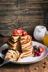 Homemade pancakes with spelt and oat flour served with fresh strawberries, cranberries, blueberries, honey and nuts. Rustic style