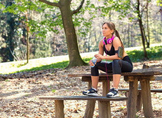 Naklejka na ściany i meble Young foman sitting on bench at the park and relaxing after jogging