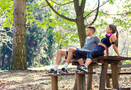 Young couple sitting on bench at the park and relaxing after jogging.