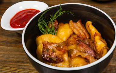 Dumplings with potatoes and bacon in a bowl on a wooden table