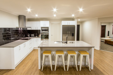 A stunning white modern kitchen with stone bench tops, tiled black splash back, black tap, stainless steel appliances and wooden flooring