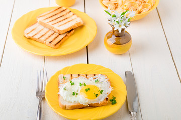 Toast with egg in yellow plate near vase with flower on white wooden background. Healthy breakfast.