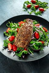 Smoked Mackerel Salad with tomato, chopped red onion, Ruccola on black plate.