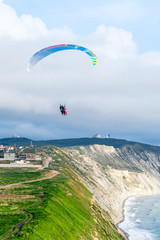 Flying tandem paragliders over the sea close to mountains, vertical view of the landscape
