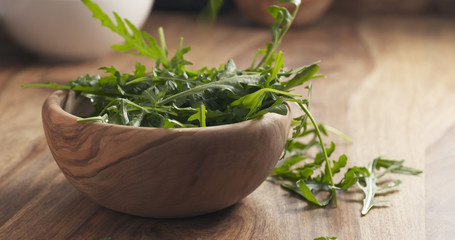 Fototapeta premium washed arugula leaves falling into the bowl on wooden table, 4k photo