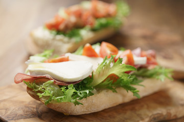 open sandwich with prosciutto, mozzarella and tomatoes on kitchen table, shallow focus