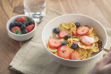 female teen girl hand eats healthy breakfast with corn flakes and berries, slightly toned photo