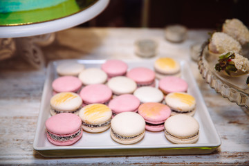 Colorful macaroons on pink table with defocused spring flowers and tea cup on background. Shallow focus