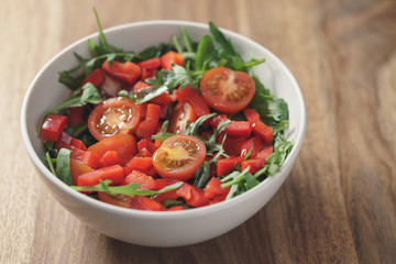 cherry tomatoes with arugula salad in white bowl on wooden table, vintage toned photo