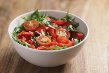 cherry tomatoes with arugula salad in white bowl on wooden table