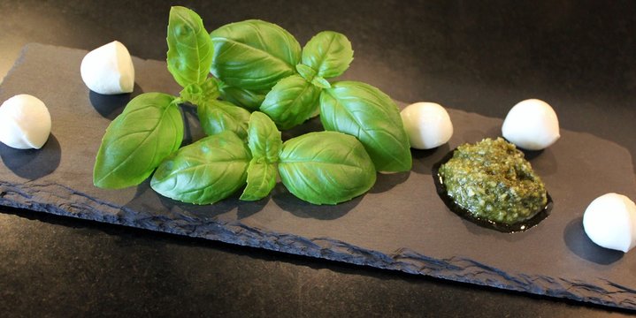 Mozzarella cheese, basil and green pesto arranged on black slate plate with black background