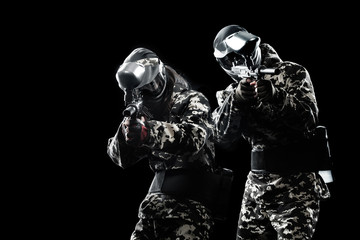 Heavily armed masked paintball soldier isolated on black background. Ad concept.