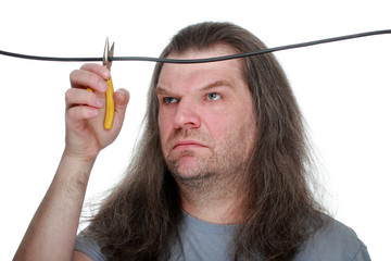 An adult man with long hair snacks the wire with wire cutters, grimacing his face.