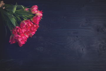 Bouquet of fresh bright pink tulips on black wooden background with copy space, retro toned