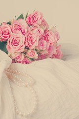 Female white dress and jewellery with fresh roses bouquet on chair, retro toned