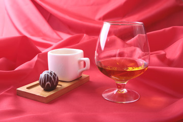 White cup of coffee and cognac in a glasses, pralines on red background.