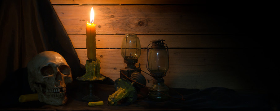 Skull with candles and barn lanterns on black cloth and old wooden wall / Still life image and selective focus, visual art

