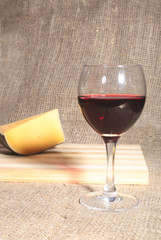 Bottle and Glass with red wine grapes and chees on wooden table.