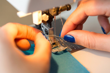 needlework and quilting in the workshop of a tailor - close-up on fingers of tailor female with blue manicure sticking thread in a needle of sewing machine