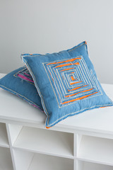 textile two blue pillows on a white background, the pillows are decorated with stitching and designer decors in the form of a labyrinth cut in the fabric through which visible multicolored lining
