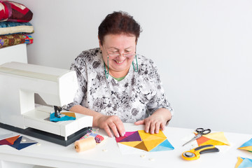 needlework and quilting in the workshop of a tailor woman - elderly smiling women put on the desktop the pieces of colored tissue, lay next to the scissors, buttons, pins and thread, rotary cutters