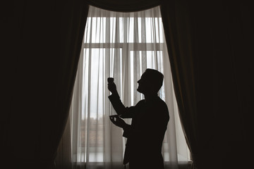 Man's silhouette at the window with cup in hand