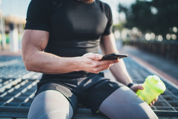 Muscular handsome athlete checking burned calories on smartphone application and smart watch after...