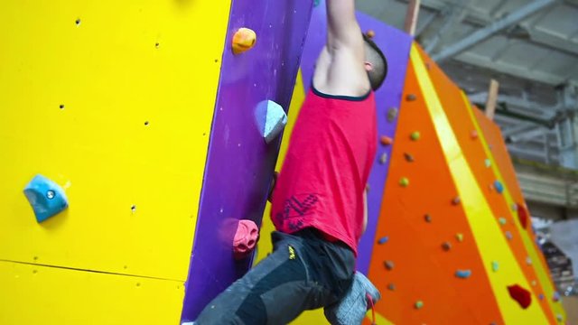 Muscular Climber Man Climbing Up On Color Rock Wall In Gym