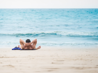 Fototapeta na wymiar Man laying on the beach enjoying summer holidays looking at the ocean