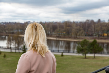 The girl with golden hair in a coat admiring the city view
