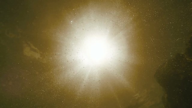 Underwater footage: sunbeams pierce the surface, air bubbles hover